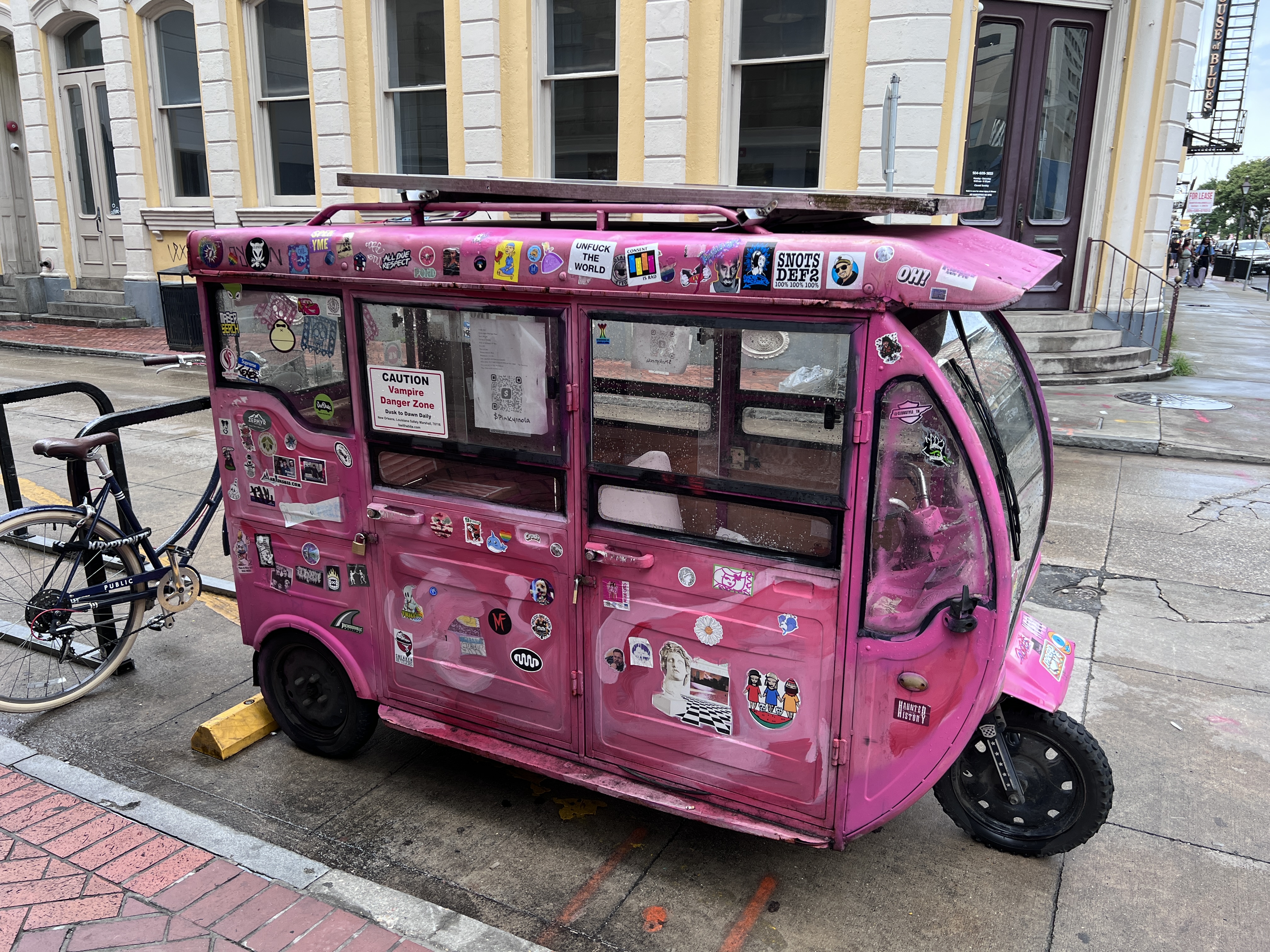 Photo of a pink tuk-tuk with stickers parked in New Orleans